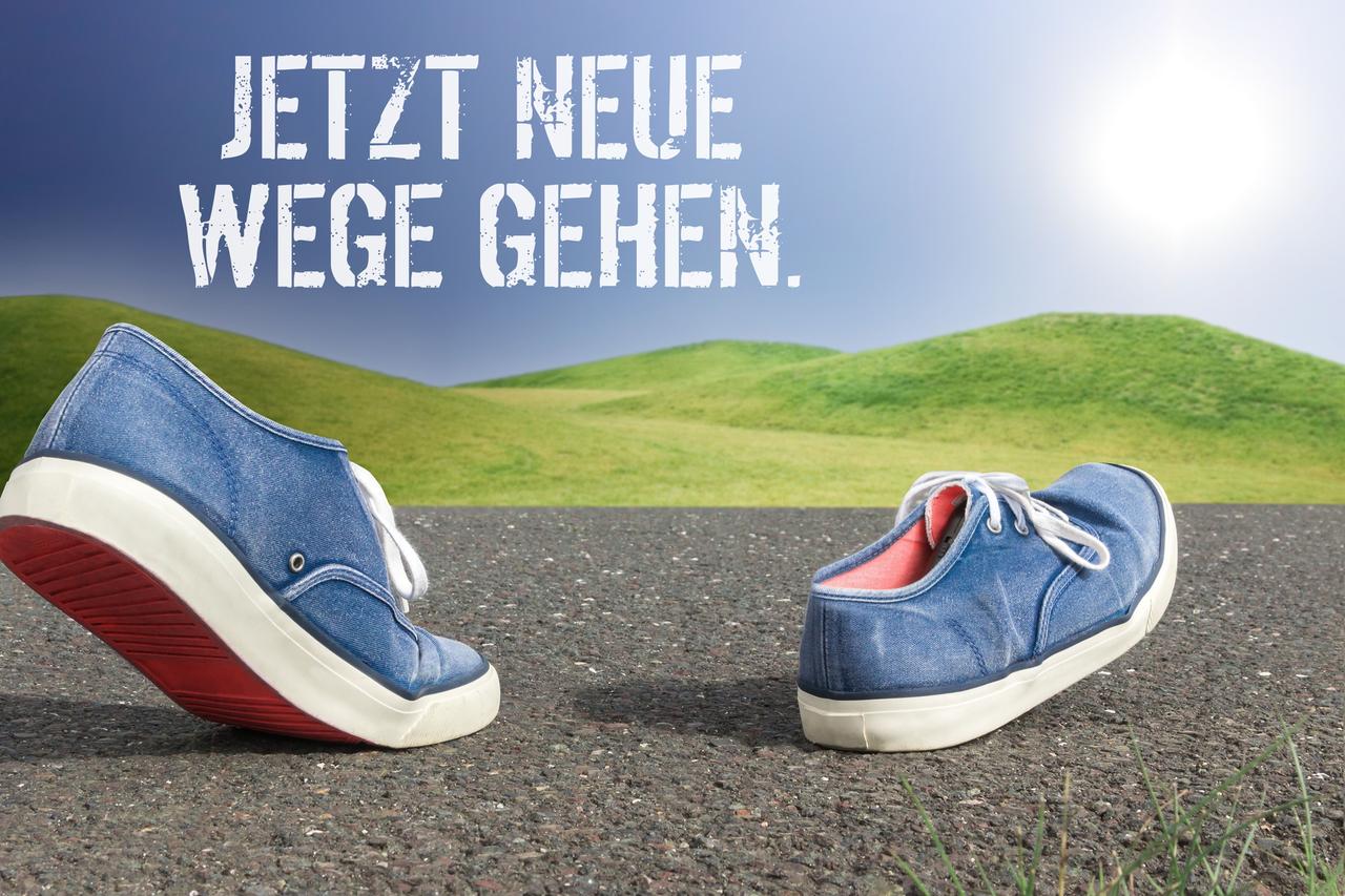 Schuhe laufen über eine asphaltierte Straße Schriftzug jetzt neue Wege gehen