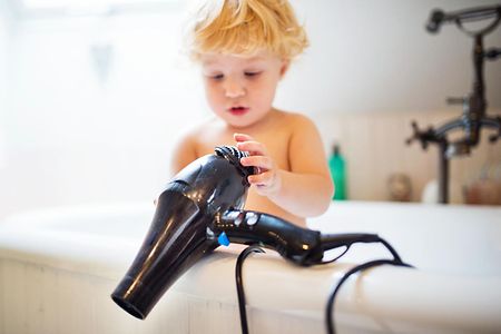 Toddler boy with hairdryer in the tub in the bathroom.